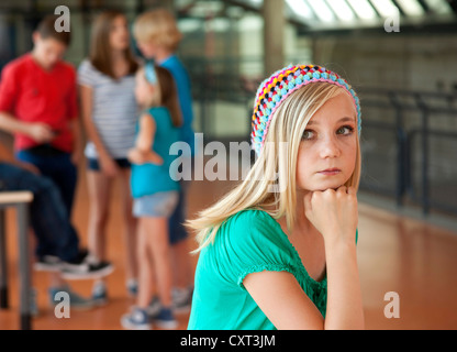 Allievi di un edificio scolastico, una ragazza guardando triste e isolato dagli altri Foto Stock