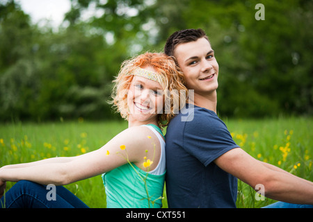 Sorridente coppia giovane seduta di schiena su un prato Foto Stock