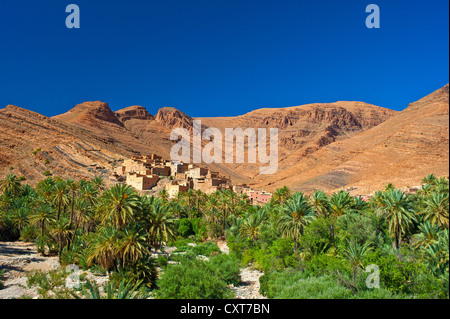 Piccolo villaggio di argilla e un boschetto di palme di fronte al rosso paesaggio di montagna in Ait Mansour valley, Anti-Atlas montagne Foto Stock