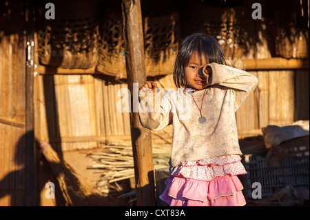 Ragazza in piedi di fronte ad una capanna di paglia, villaggio di Akha hill tribe, minoranza etnica, nei pressi di Santikhiri o Mae Salong Foto Stock