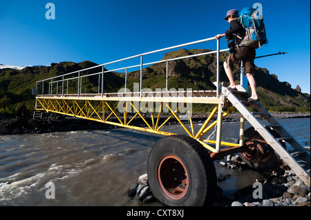 Femmina di escursionisti a piedi su un ponte mobile attraverso il glaciale Krossá river, sentiero escursionistico al Fimmvoerðuháls alta pianura Foto Stock