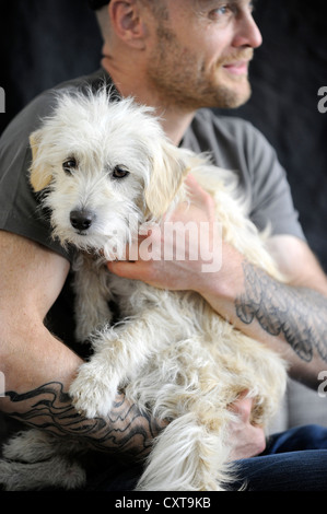 Mongrel terrier, un anno, tra le braccia del suo tatuato proprietario Foto Stock