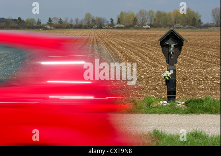 Commemorative croce sul ciglio della strada per la vittima di un incidente, con auto velocizzando il passato, country road vicino a Anzing, Alta Baviera, Baviera Foto Stock