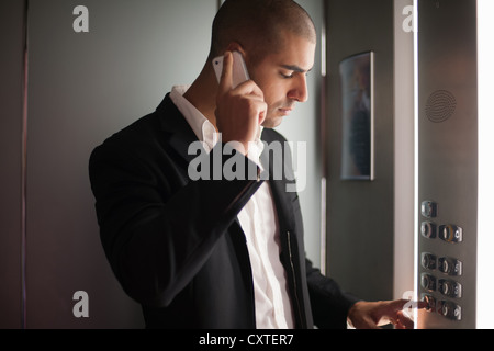 Imprenditore sul telefono cellulare in ascensore Foto Stock