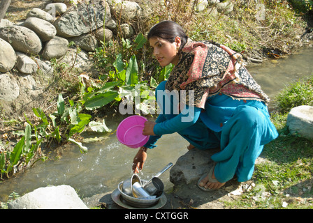 Un abitante locale lavaggio piatti in una piccola corrente passante in un villaggio nei pressi di Pahalgam Foto Stock