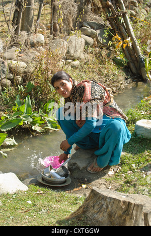 Un abitante locale lavaggio piatti in una piccola corrente passante in un villaggio nei pressi di Pahalgam Foto Stock