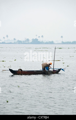 Vista verticale tradizionale di un pescatore nella sua barca da pesca su le lagune del Kerala, la pesca dei mitili. Foto Stock