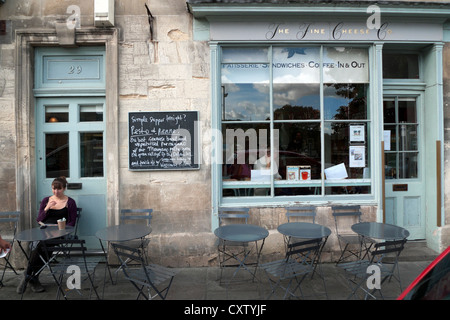 Una donna seduta al di fuori delle belle Cheese Company su Walcot Street nella città di Bath Spa, Avon, Somerset, Inghilterra, Regno Unito Foto Stock