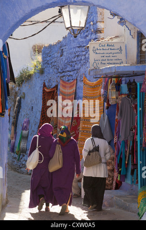 Chefchaouen, Chefchaouen Provincia, Marocco. Tipica scena nella medina. Tre donne in abbigliamento locale a piedi dal negozio Foto Stock