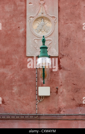 Un veneziano tipico lampione davanti a una scultura in pietra raffigurante un housefly entro un cerchio sul lato di una casa Foto Stock