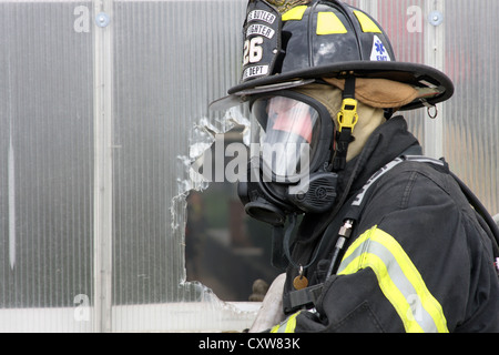 Un vigile del fuoco alimentando una hoseline attraverso un foro nella parete Foto Stock