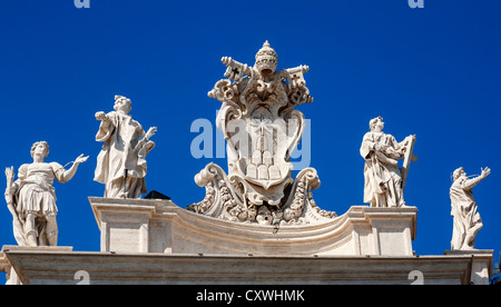 Stemma papale e statue in cima alla Basilica di San Pietro e la Città del Vaticano, Roma, Italia. Foto Stock