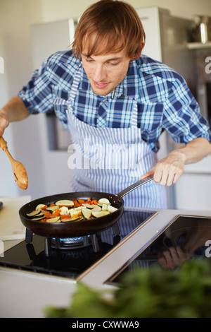 L'uomo friggere ortaggi in cucina Foto Stock
