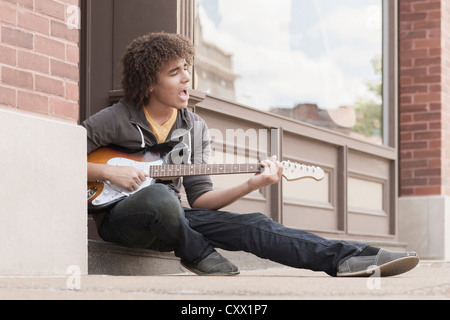 Razza mista adolescente suonare la chitarra elettrica e canto Foto Stock