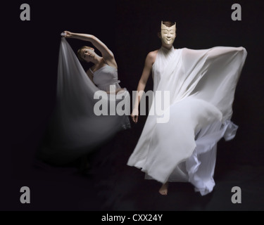 Due ballerine in flusso di camici bianchi eseguire sotto illuminazione drammatica in mezzo a un sfondo nero Foto Stock