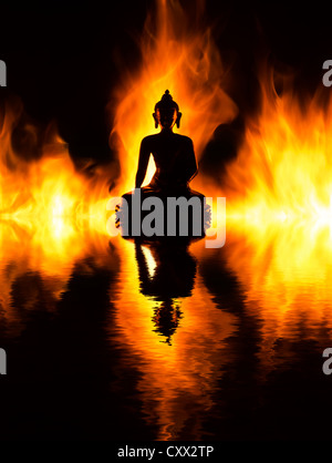 Statua del Buddha davanti al fuoco con la riflessione contro uno sfondo scuro Foto Stock