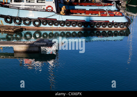 Riflesso nell'acqua di due rimorchiatori ormeggiato a fianco di ogni altro, Portsmouth, Inghilterra. Foto Stock