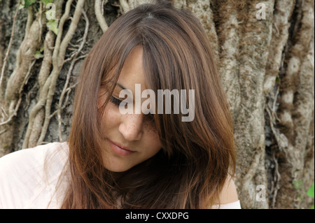 Considerato giovane donna di origine indonesiana, ritratto, seduti nella parte anteriore del tronco di un albero, publicground Foto Stock