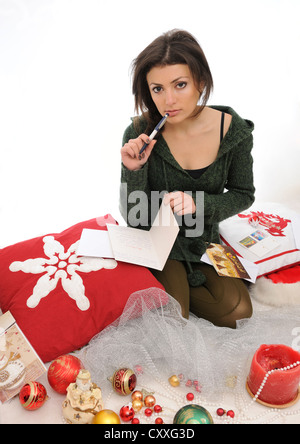 Giovane donna scrivere cartoline di Natale tra le decorazioni di Natale Foto Stock