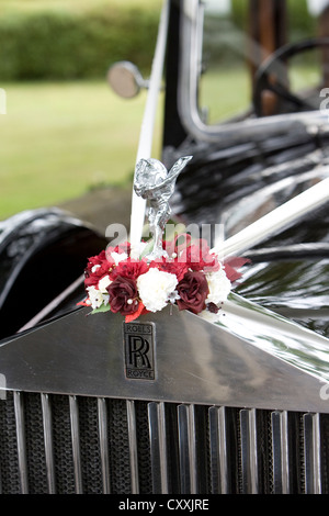 Rolls Royce classic vintage dettaglio auto che mostra una parte della griglia anteriore, badge e spirito di ecstasy statua d'argento inanellati da fiori Foto Stock