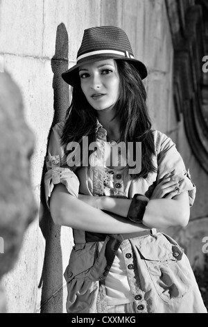 Donna che indossa un cappello e un cappotto, in piedi di fronte a un muro di pietra Foto Stock