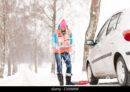 Donna che mantiene catene per pneumatici vettura rotto di neve in inverno i problemi dei giovani Foto Stock