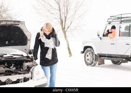 Donna che guarda sotto rotto cofano auto neve problemi assistenza man Foto Stock