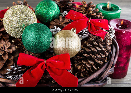 Holiday cestello contenente i nastri rosso secco, pigne, oro e ornamenti di verde e le candele con la fiamma in background Foto Stock
