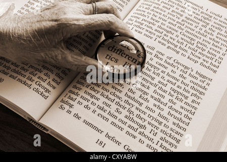 Signora anziana con ipovedenti con lente di ingrandimento per leggere il grande libro di stampa Foto Stock