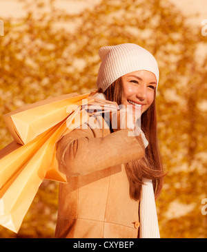 Foto della bella ragazza con shopping bag, closeup ritratto di donna attraente isolato sul fogliame di autunno sfondo Foto Stock