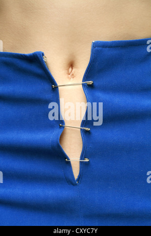 Donna che indossa un mantello con una cerniera rotta tenuti insieme con le spine di sicurezza, close-up di un pulsante di emergenza Foto Stock