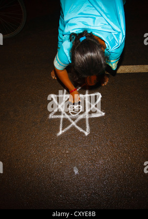 Donna in Sari piegato verso il basso disegno Disegno Kolam per una cerimonia in strada, Trichy, India Foto Stock