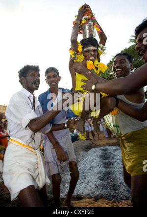 Ragazzino con abiti di colore giallo portato da uomini riuscendo a camminare sul fuoco in Tamil Nadu, Madurai, in India del Sud Foto Stock