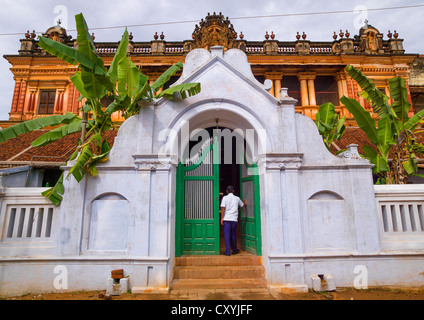 L'uomo l'apertura del portale di un vecchio palazzo Chettiar con alberi di banana e intagli di immagine indù, Kanadukathan Chettinad, India Foto Stock