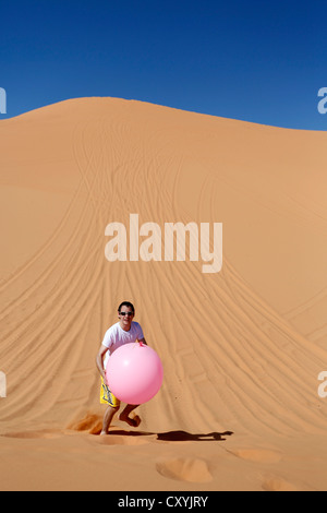 Leggerezza, uomo che porta un grande palloncino rosa nel deserto, Coral Pink Sand Dunes State Park, vicino a Kanab, Utah, Stati Uniti d'America Foto Stock