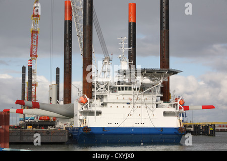 Nave utilizzata per la costruzione di parchi eolici offshore lascia Eemshaven portante una testa di turbina eolica, guidato da barche rimorchiatore. Foto Stock