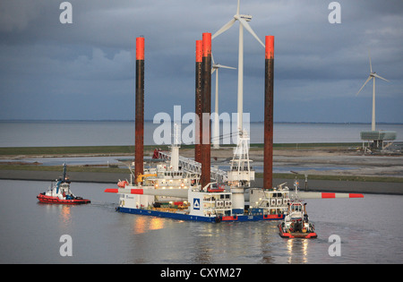 Nave utilizzata per la costruzione di parchi eolici offshore lascia Eemshaven portante una testa di turbina eolica, guidato da barche rimorchiatore. Foto Stock