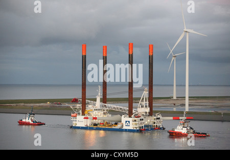 Nave utilizzata per la costruzione di parchi eolici offshore lascia Eemshaven portante una testa di turbina eolica, guidato da barche rimorchiatore. Foto Stock