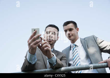 Giovane imprenditore controllando il suo telefono mobile e mostrando qualcosa a un collega Foto Stock
