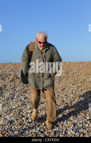 Anziani uomo a camminare con attenzione sulla spiaggia ghiaiosa Foto Stock