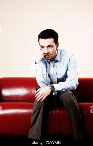 Giovane uomo pensively seduta su un divano e in attesa Foto Stock