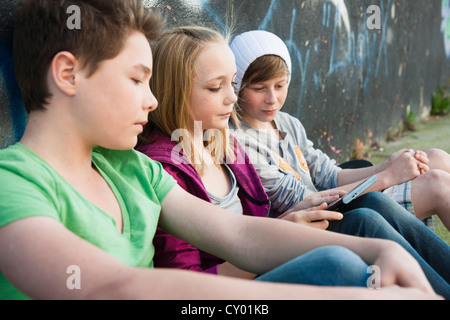 Tre adolescenti con un tablet PC seduti di fronte a un muro con graffiti Foto Stock