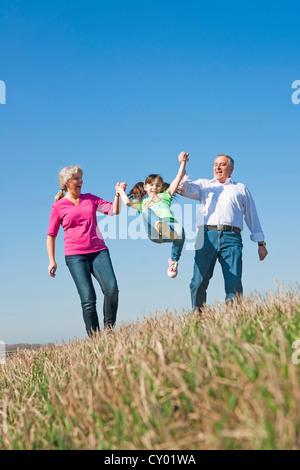 Nonni swinging loro nipote in aria con le loro mani Foto Stock