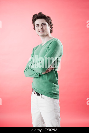 Giovane uomo che indossa un maglione verde casualmente in piedi di fronte ad una parete rossa Foto Stock