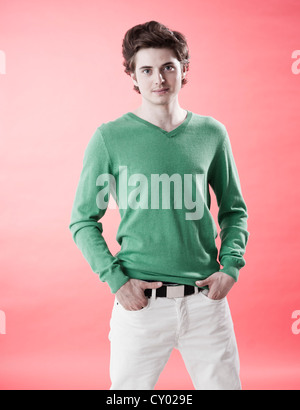 Giovane uomo che indossa un maglione verde casualmente in piedi di fronte ad una parete rossa Foto Stock
