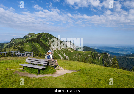 Donna seduta su una panca in legno godendo la vista dalla cima del monte Bauneck, Bavaria Foto Stock
