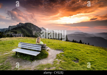 Donna seduta su una panca in legno godendo la vista dalla cima del monte Bauneck, Bavaria Foto Stock