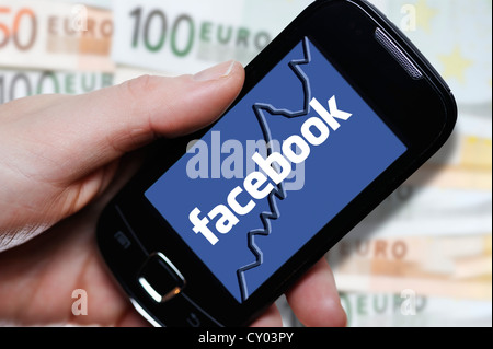 Mano che tiene uno smartphone con un logo di Facebook nella parte anteriore delle banconote, immagine simbolica per la IPO di Facebook Foto Stock