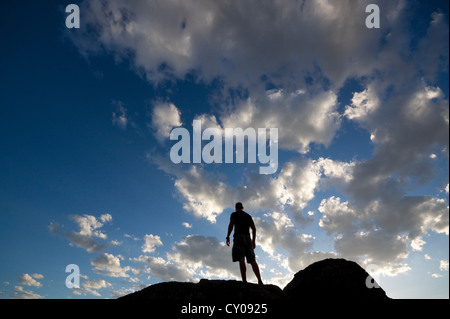 Silhouette di figura maschile in piedi sulla roccia contro il cielo blu Foto Stock