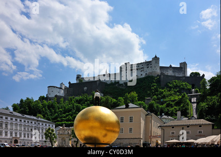 Vista del castello di Hohensalzburg come visto dalla piazza Kapitelplatz, una statua di un uomo che indossa pantaloni neri e una camicia bianca in piedi Foto Stock